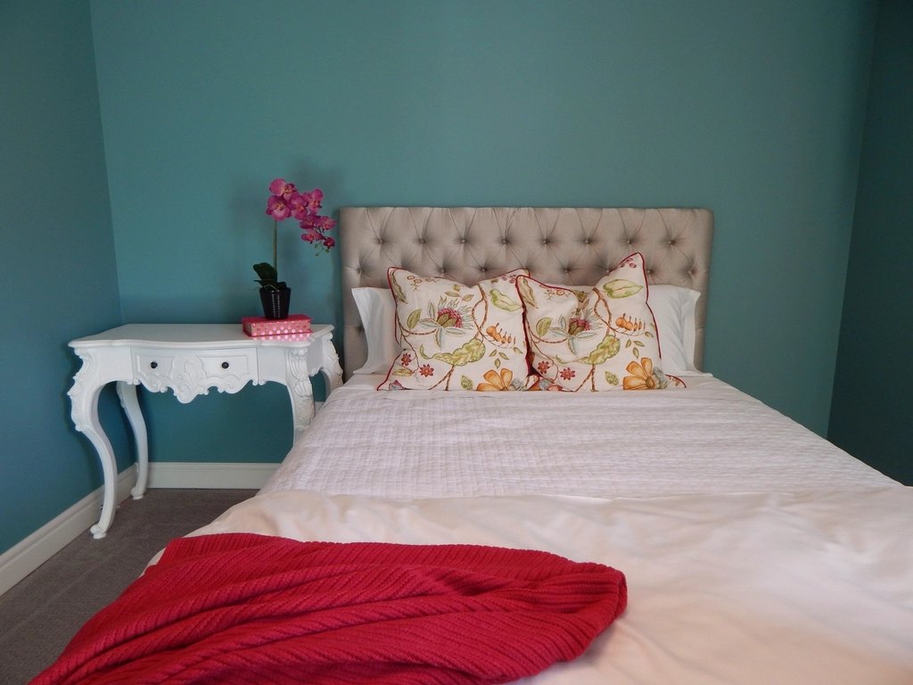 Cream buttoned/tufted upholstered divan bed against a teal wall